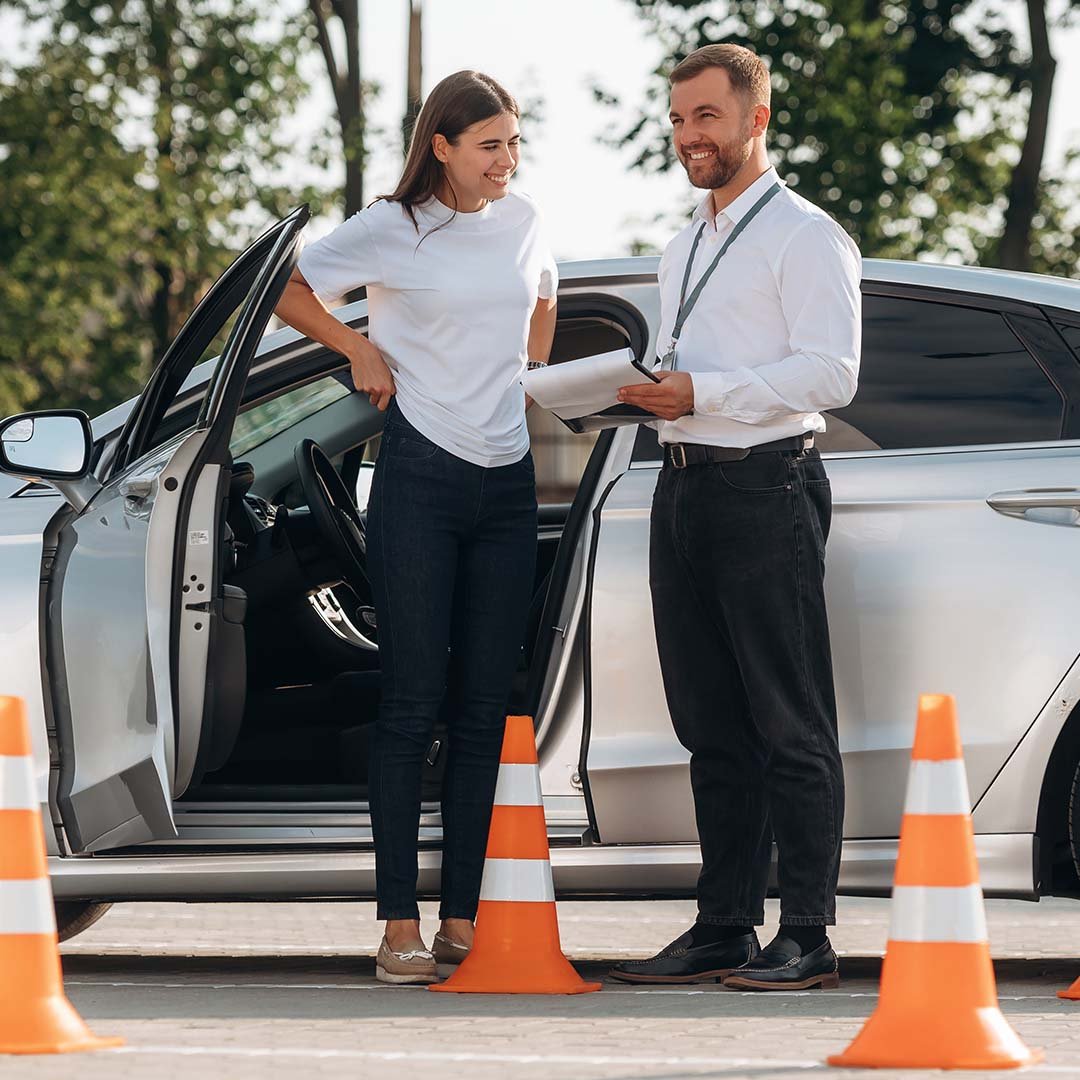 Driving lesson instructor coaching learner beside car with cones